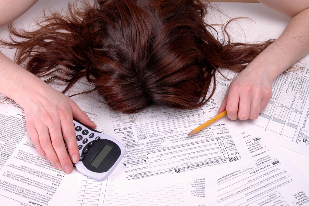 Woman slumped over a pile of tax forms with a calculator and pencil in hand.